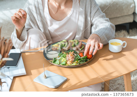 Stylish young Asian woman eating at the living room table 137365673