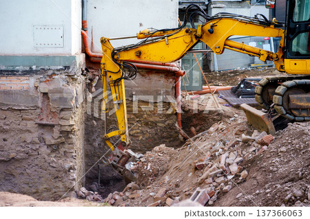 Hydraulic excavator clearing debris near building foundation. Renovation project, engineering work and industrial development theme. Hydraulic excavator clearing debris near building foundation. Renovation project, engineering work and industrial development theme. 137366063