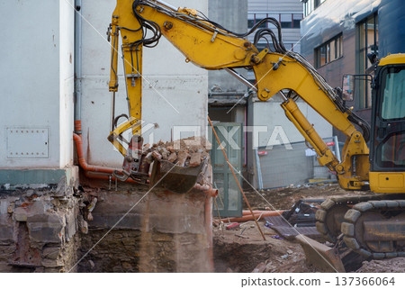 Yellow excavator removing concrete and bricks during demolition. Urban redevelopment, heavy machinery and construction industry concept. Yellow excavator removing concrete and bricks during demolition. Urban redevelopment, heavy machinery and construction industry concept. 137366064