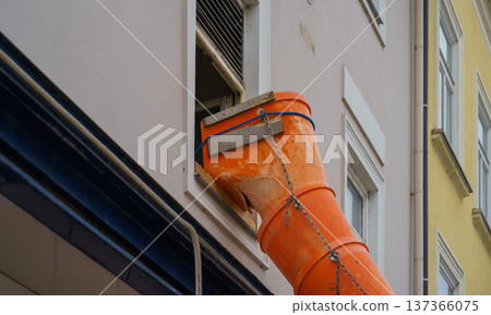 Orange debris chute attached to upper floor window for construction waste removal. Urban renovation, safety equipment, building modernization concept Orange debris chute attached to upper floor window for construction waste removal. Urban renovation, safety equipment, building modernization concept 137366075