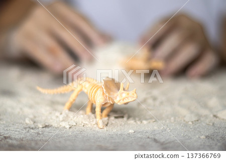 A toy dinosaur skeleton stands on a table against the backdrop of children's hands. 137366769
