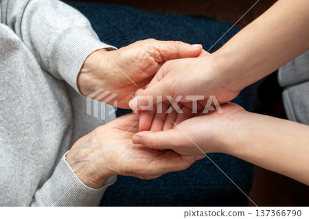 Young caregiver holding elderly person's hands showing compassion and support in home care Young caregiver holding elderly person's hands showing compassion and support in home care 137366790