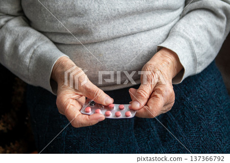 Senior holding a blister pack of pink pills in hand at home, representing medication and elderly care Senior holding a blister pack of pink pills in hand at home, representing medication and elderly care 137366792