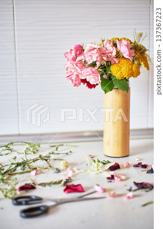 Fresh flower bouquet in a bamboo vase on a counter with petals and scissors. Home floral arrangement and DIY craft. Celebration and decor. Fresh flower bouquet in a bamboo vase on a counter with petals and scissors. Home floral arrangement and DIY craft. Celebration and decor. 137367223