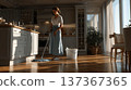 Woman Mopping Floor in Bright Modern Kitchen, Sunlight Filtering Through Large Windows Creating Warm 137367365