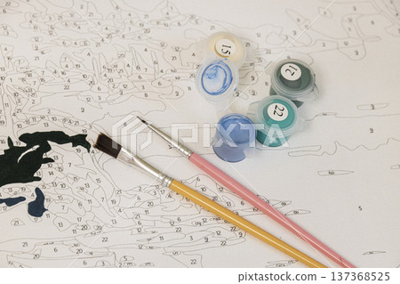 Detailed shot of a paint-by-numbers canvas with numbered sections and paint containers. The image shows the organized creative process of coloring a pre-drawn sketch. 137368525