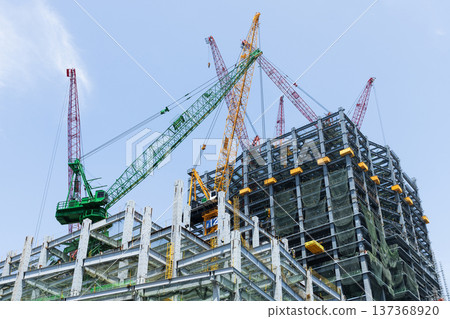 Low-angle view of cranes and steel structures of building construction with a blue sky background in Taiwan. Low-angle view of cranes and steel structures of building construction with a blue sky background in Taiwan. 137368920