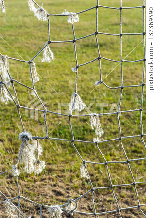 Torn soccer net displaying wear and tear in a grassy field during daylight hours Torn soccer net displaying wear and tear in a grassy field during daylight hours 137369590