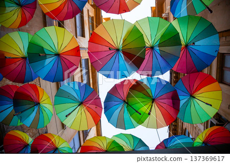 Colorful umbrellas suspended above a charming street create a vibrant and cheerful atmosphere in the heart of a lively town Colorful umbrellas suspended above a charming street create a vibrant and cheerful atmosphere in the heart of a lively town 137369617