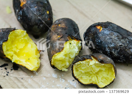 Grilled sweet potatoes served on a rustic wooden surface with a focus on their charred skin and fluffy interior 137369629