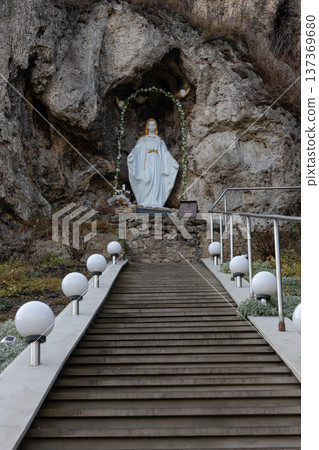 Stairway leading to a serene statue of a religious figure nestled in rocky terrain surrounded by softly glowing orbs at dusk 137369680