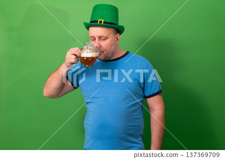Man in green leprechaun hat drinking frothy beer from glass. St. Patricks Day celebration with Irish pub tradition. Festive holiday enjoyment and cultural cheer. photography Man in green leprechaun hat drinking frothy beer from glass. St. Patricks Day celebration with Irish pub tradition. Festive holiday enjoyment and cultural cheer. photography 137369709