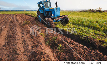 Blue tractor plowing the field creating furrows in the soil 137370919