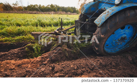 Blue tractor plowing the field in autumn, creating furrows in the soil 137370920