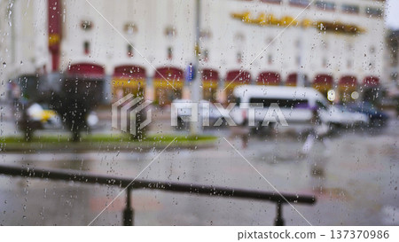 Raindrops on glass seeing out of focus city street with cars and buildings on a wet day Raindrops on glass seeing out of focus city street with cars and buildings on a wet day 137370986