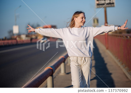 Young woman balancing on a bridge railing with arms open embracing freedom 137370992