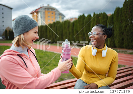 Diverse friends laughing and sharing water on sports track 137371379