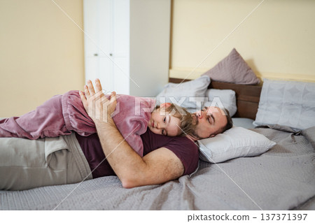 Father and young daughter sleeping on bed embracing 137371397