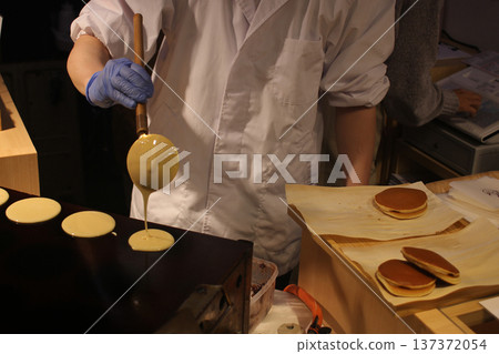 closeup Chef's hands Cooking Japanese Mini Pancakes (Dorayaki batter or castella-style cakes) on Hot Griddle at Food Stall in Sapporo, Japan  137372054