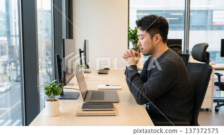 Businessman Praying at Office Desk by Window 137372575