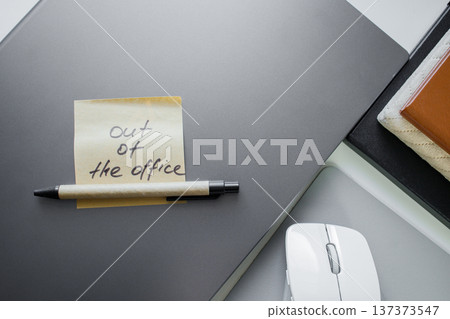 Office job style flat lay. Sticky note with handwritten phrase out of office on a laptop with pen, notebooks and computer mouse . Temporarily unavailable concept, vacation, business trip or day off 137373547