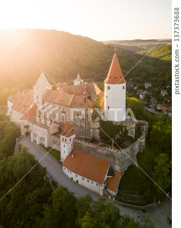 Krivoklat Castle, located in Central Bohemia, displays its medieval charm as the sun sets behind the hills, casting a warm glow over the ancient structure and surrounding landscape. 137373688