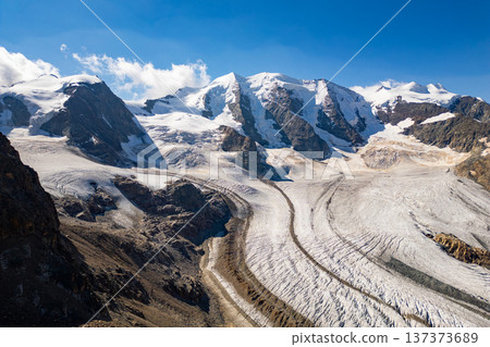 Piz Palu towers high over the Pers Glacier, showcasing the breathtaking beauty of the Swiss Alps. The rocky ridges contrast with the smooth glacier surface under a clear blue sky. Piz Palu towers high over the Pers Glacier, showcasing the breathtaking beauty of the Swiss Alps. The rocky ridges contrast with the smooth glacier surface under a clear blue sky. 137373689