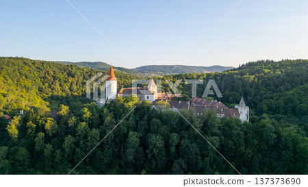 Krivoklat Castle stands proudly amidst lush green forests in Central Bohemia. Captured during sunset, the medieval architecture glows warmly against the twilight sky. Krivoklat Castle stands proudly amidst lush green forests in Central Bohemia. Captured during sunset, the medieval architecture glows warmly against the twilight sky. 137373690