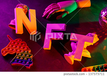 Colorful nft letters with neon pop it fidget toys and disco ball on dark surface 137373711