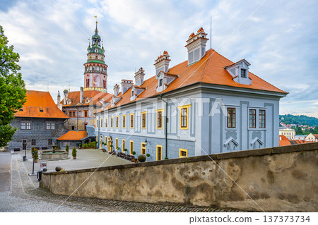 Visitors explore Cesky Krumlov Castle in the summer. The historic architecture stands tall against the sky. Trees and paths create a scenic setting for tourists enjoying the view. Visitors explore Cesky Krumlov Castle in the summer. The historic architecture stands tall against the sky. Trees and paths create a scenic setting for tourists enjoying the view. 137373734