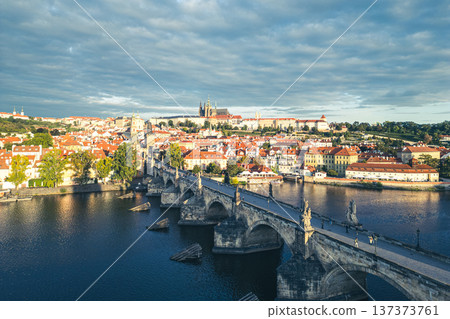 The beauty of Prague Castle and Charles Bridge at dawn. The sun rises over the Vltava River, illuminating the historic buildings and creating a serene atmosphere. 137373761
