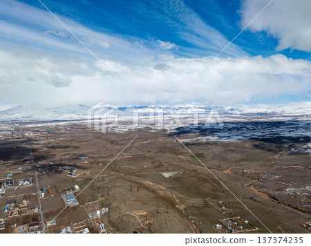 Snowy mountain range overlooks a dry valley with small settlements Snowy mountain range overlooks a dry valley with small settlements 137374235
