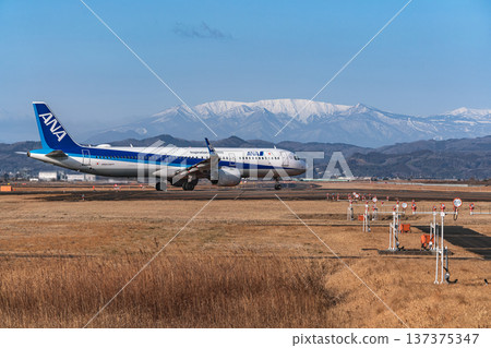 A passenger plane takes off from Sendai Airport towards the snow-capped Zao mountain range. 137375347