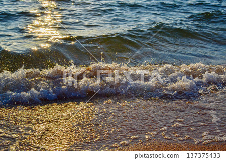 Waves on the sandy shore in the rays of sunset dawn 137375433