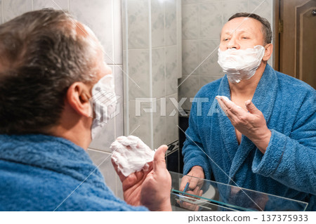 Mature man applying shaving foam in bathroom mirror morning grooming routine Mature man applying shaving foam in bathroom mirror morning grooming routine 137375933