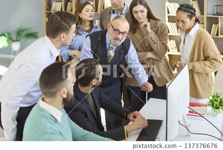 Senior mentor guiding adult students around computer in office training session 137376676