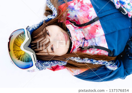 一位身穿滑雪服的年輕女子在雪坡上玩雪。 137376854