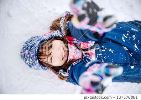A young woman wearing ski wear playing with snow on the slopes 137376861