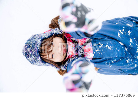 A young woman wearing ski wear playing with snow on the slopes A young woman wearing ski wear playing with snow on the slopes 137376869