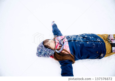 A young woman wearing ski wear playing with snow on the slopes A young woman wearing ski wear playing with snow on the slopes 137376872