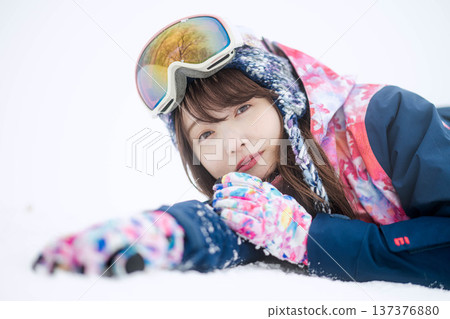 一位身穿滑雪服的年輕女子在雪坡上玩雪。 137376880