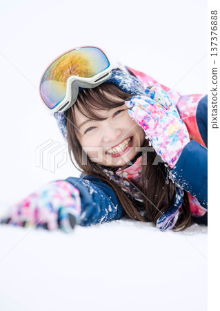 A young woman wearing ski wear playing with snow on the slopes 137376888