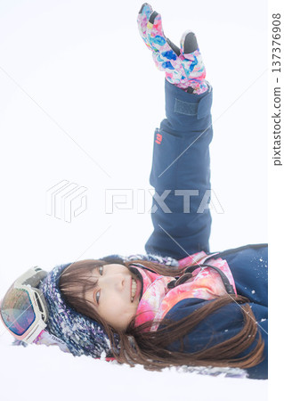 一位身穿滑雪服的年輕女子在雪坡上玩雪。 137376908