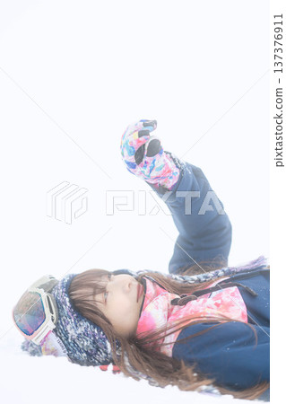 A young woman wearing ski wear playing with snow on the slopes A young woman wearing ski wear playing with snow on the slopes 137376911