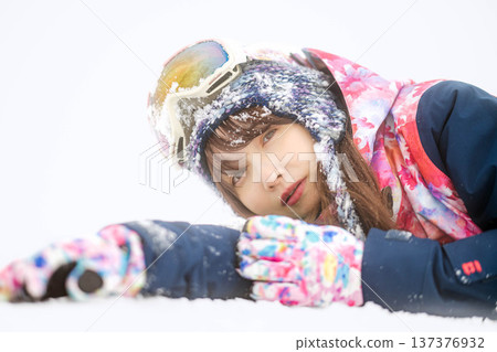 A young woman wearing ski wear playing with snow on the slopes A young woman wearing ski wear playing with snow on the slopes 137376932