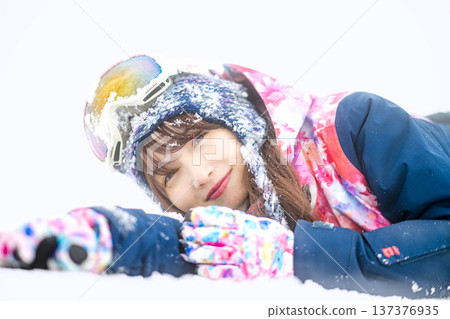 A young woman wearing ski wear playing with snow on the slopes A young woman wearing ski wear playing with snow on the slopes 137376935