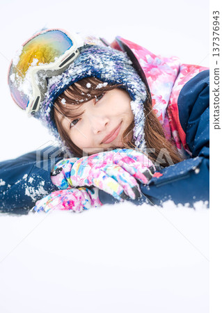 A young woman wearing ski wear playing with snow on the slopes 137376943