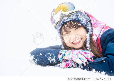 A young woman wearing ski wear playing with snow on the slopes A young woman wearing ski wear playing with snow on the slopes 137376945