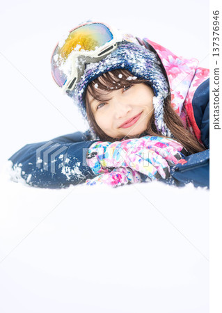 A young woman wearing ski wear playing with snow on the slopes 137376946