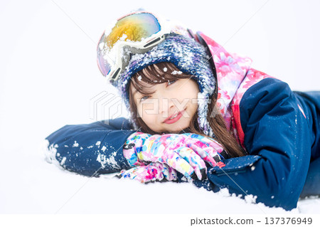 A young woman wearing ski wear playing with snow on the slopes A young woman wearing ski wear playing with snow on the slopes 137376949